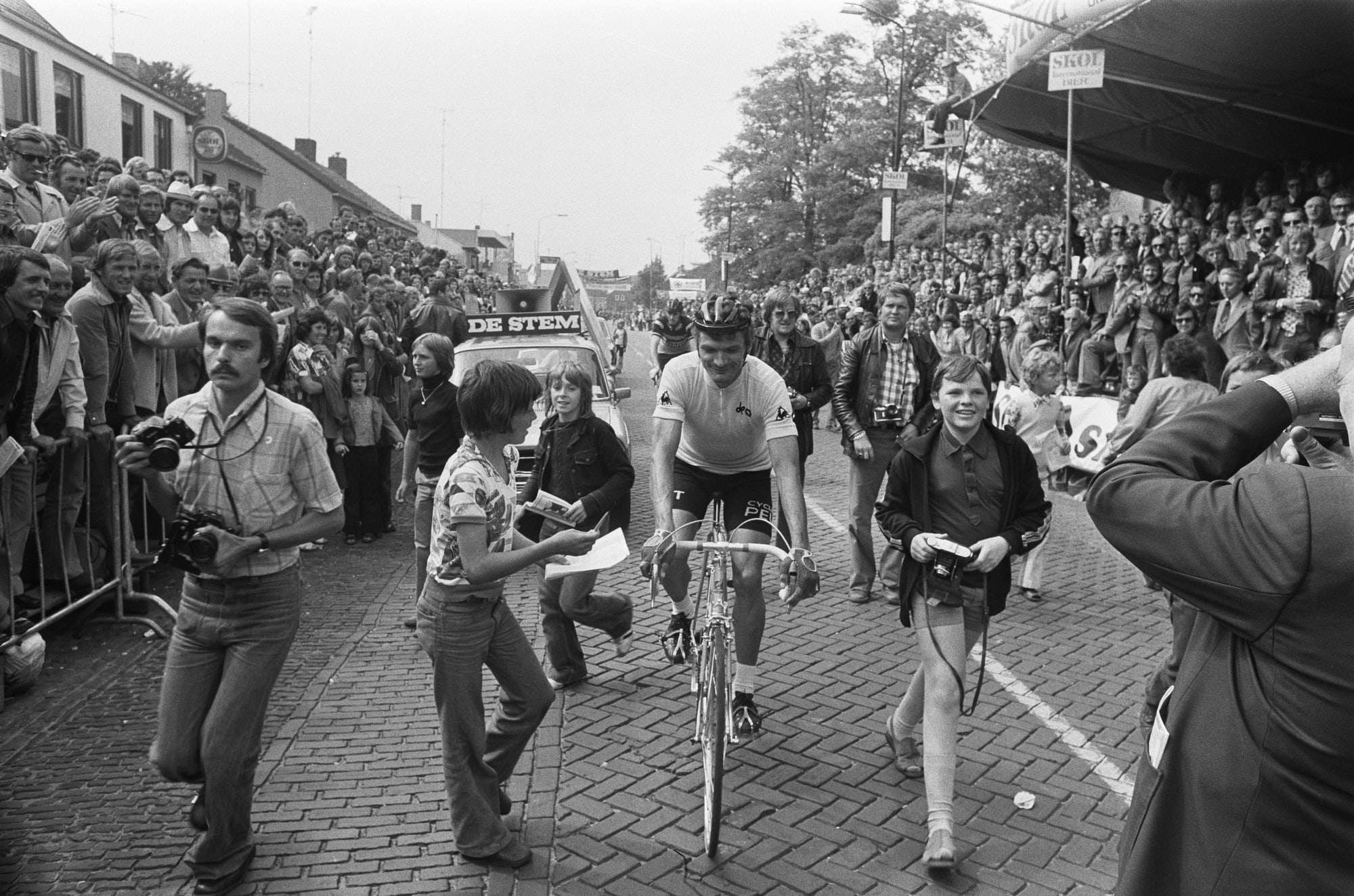 Bernard Thévenet à vélo, entouré par une foule de spectateurs sur une route pavée
