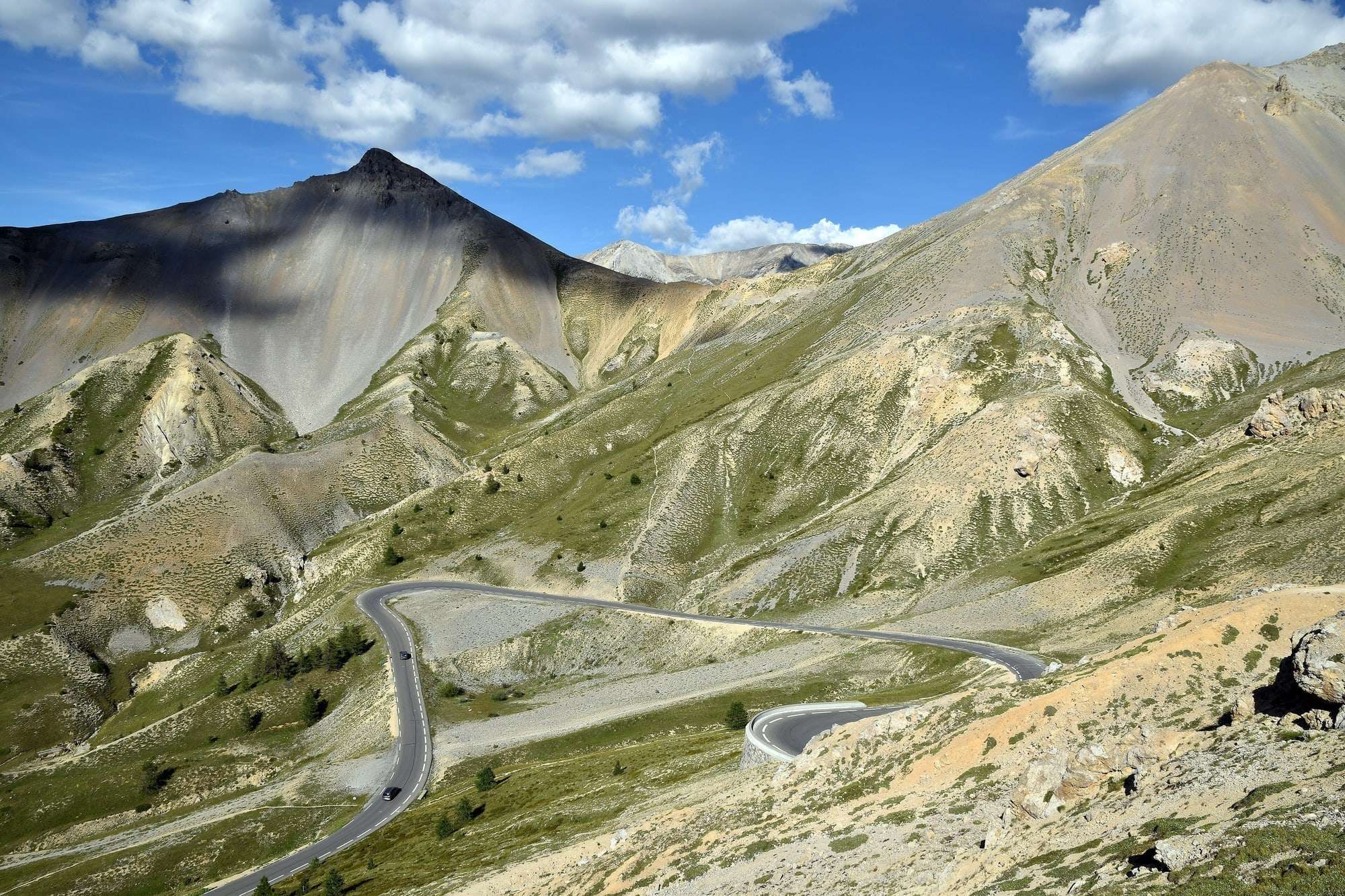 Route en lacets du col d'Izoard entre des pentes minérales, sous un ciel bleu