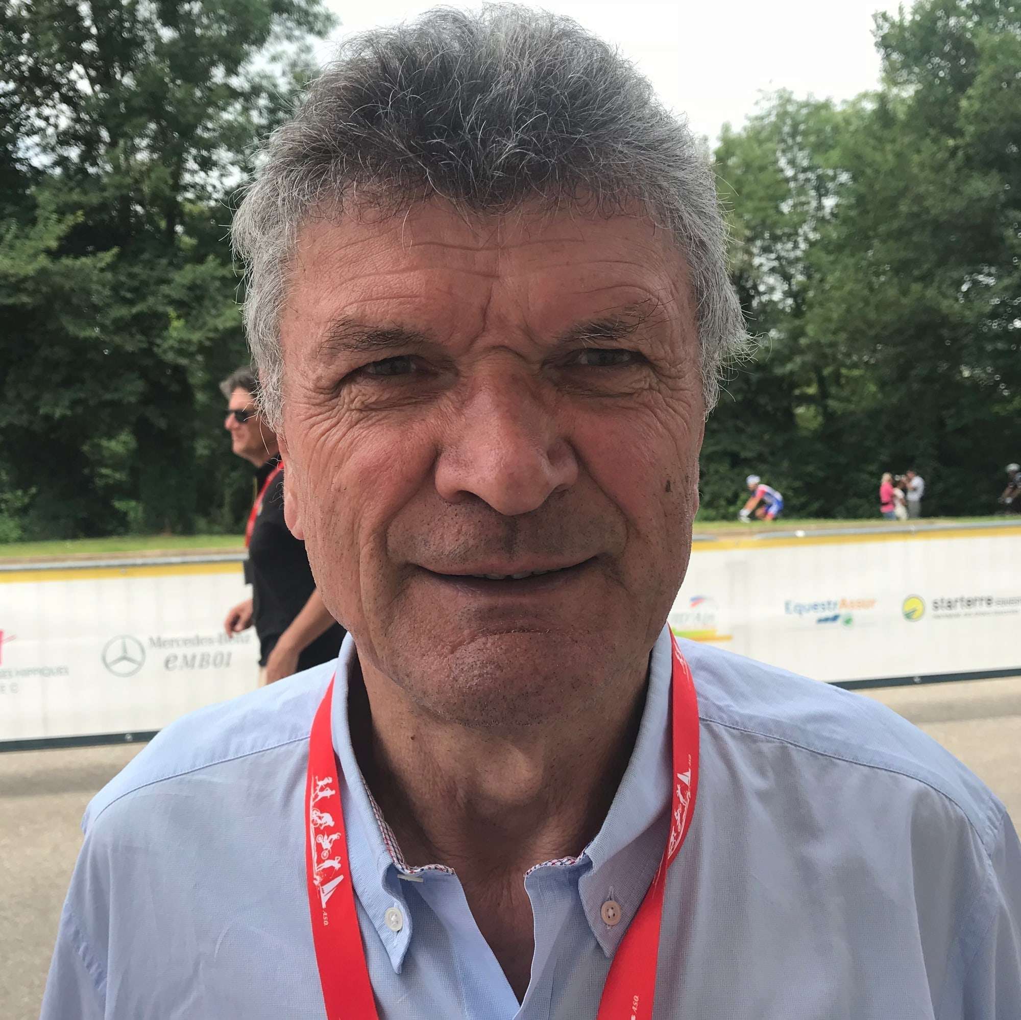 Portrait souriant de Bernard Thévenet, accréditation rouge autour du cou