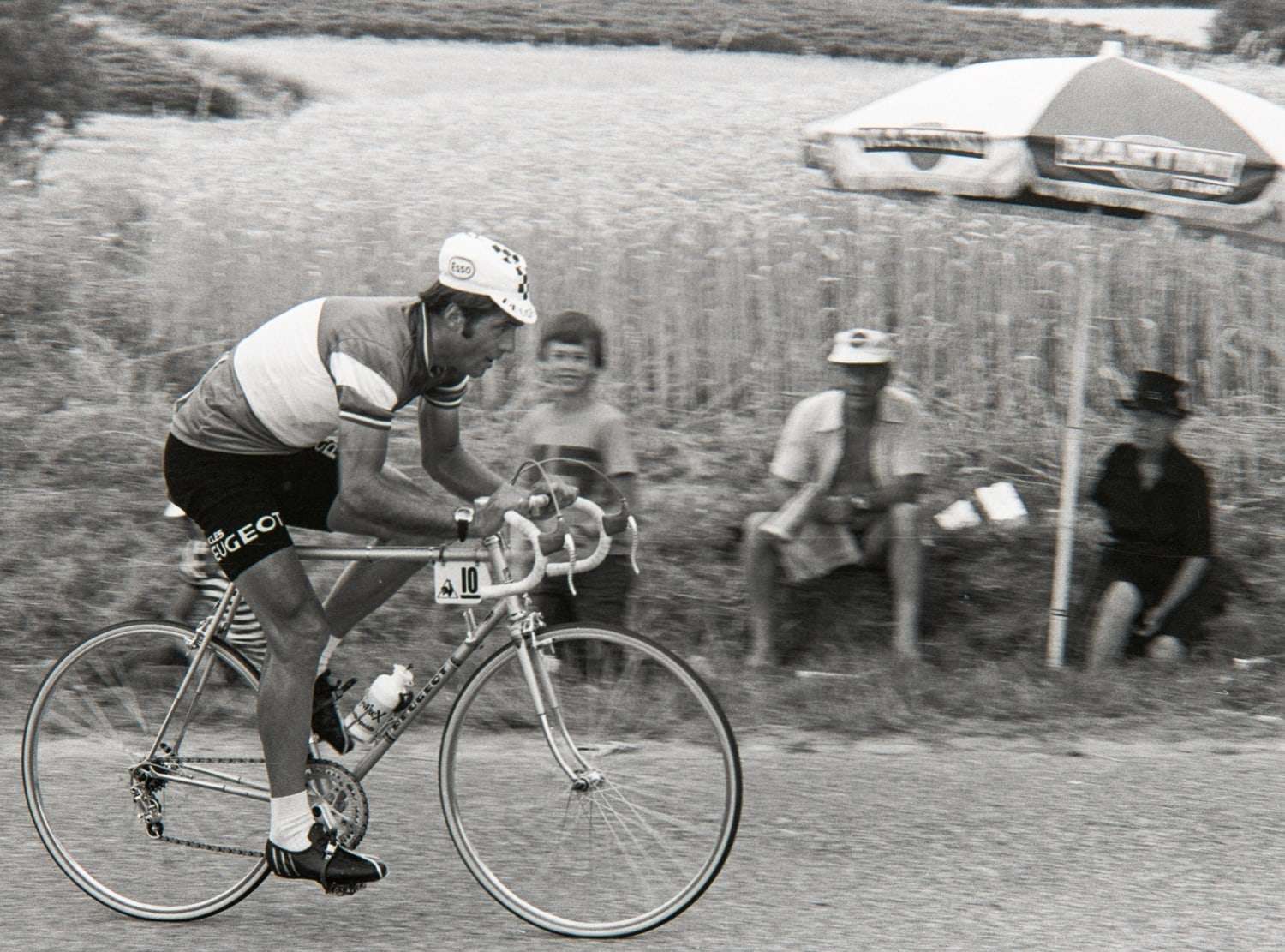 Guy Sibille en maillot Peugeot, en course devant des spectateurs assis sous un parasol
